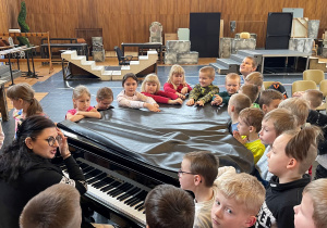 Uczniowie są zebrani przy fortepianie i biorą udział w warsztatach wokalnych.