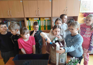 Uczniowie klas młodszych sadzą kwiatki bratki do długich doniczek.