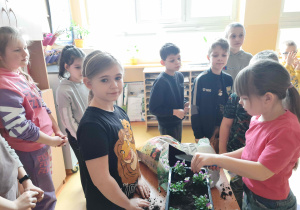 Uczniowie klas młodszych sadzą kwiatki bratki do długich doniczek.