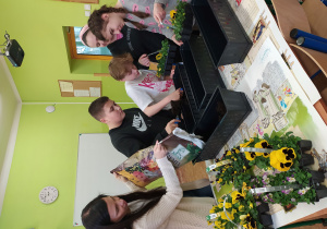 Uczniowie klas starszych sadzą kwiatki bratki do długich doniczek.