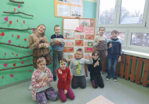 Uczniowie klasy drugiej a trzymający lizaki w kształcie serc na tle tematycznej dekoracji.