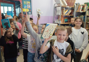 Grupa uczniów w bibliotece z wypożyczonymi książkami.