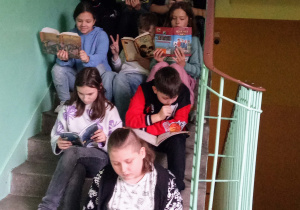 Dzieci siedzą na schodach, każde czyta swoją książkę.