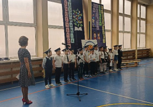 Klasa pierwsza wraz z wychowawczynią na tle świątecznej dekoracji, na sali gimnastycznej.