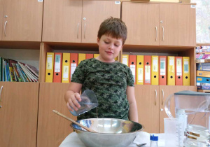 Chłopiec nalewa do metalowej miski wodę.