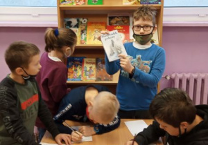 Dzieci przeglądające książki o misiach, w tle regał z wystawką książek.