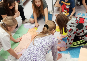 Grupa uczniów układa na podłodze mapę z puzzli.