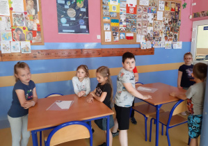 Przedszkolaki przy stolikach układają papierowe puzzle owadów.